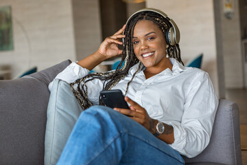 Front view of woman listening to music with headphones and using mobile phone while leaning on a sofa at home