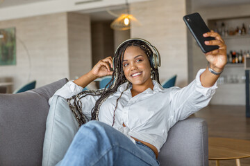 Front view of woman taking a selfie wearing headphones while leaning on a sofa at home