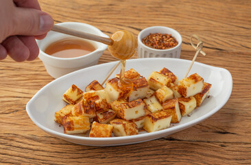 Hand pouring sugar syrup over grilled Rennet or Coalho cheese with  pepper on a wooden table