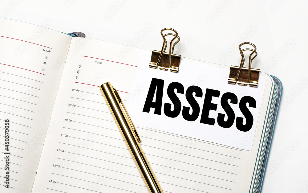 Poster on a light background, an open notebook, a sheet of paper with gold clips and the text assess and a 