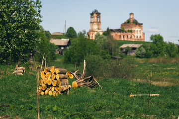 a woodpile on the background of a beautiful rural summer landscape. Houses and orthodox church. Summer village day, Russia