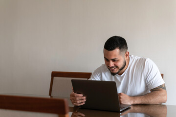 Fototapeta na wymiar Latin man smiling and looking at a laptop screen while holding it