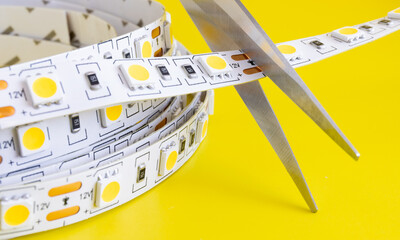 Long LED light strip tape is cut on yellow background