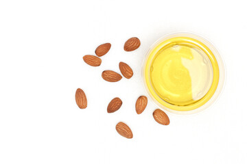 Yellow almond oil in a clear bowl and several almonds on a white background