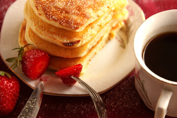 Light delicious breakfast with coffee. Delicate pancakes with sugar powder and strawberries.