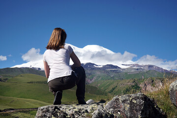 Naklejka premium a girl in the mountains looks at the mountain Elbrus
