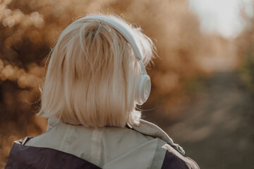Back view of caucasian young woman listening music with headphones on sunny day while walking in city park