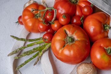 Tomatoes, asparagus, and mushrooms coming out of a fabric shopping bag