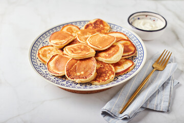 Sweet pancakes with sour cream on a plate on a white table