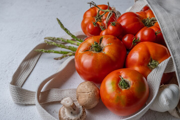 Tomatoes, asparagus, and mushrooms coming out of a fabric shopping bag