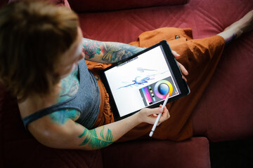 Cute red-haired girl artist draws on a tablet in a cozy living room in a real interior, top view of the tablet screen close-up,