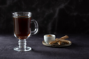Healthy hot chicory drink in the glass cup, chicory roots and crushed chicory in small white bowl on dark background. Side view