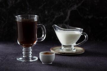 Healthy hot chicory drink in the glass cup , crushed chicory root in small white bowl and milk in glass jug on dark background. Side view
