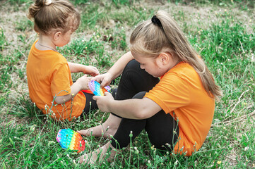 Two girls in identical T-shirts are sitting on the grass and playing 