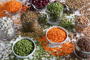 Lentils, chickpeas, chopped peas, red and white beans in multi-sized bowls on a concrete background
