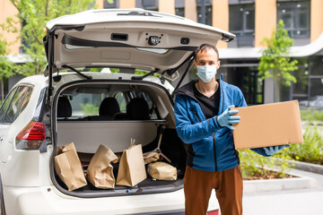 Postal delivery courier man wearing protective face mask in front of cargo van delivering package holding box due to Coronavirus disease or COVID-19