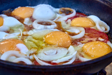 close-up of frying eggs with onions and tomatoes in a frying pan. picnic in nature