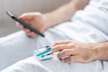 Patient lying at bed with pulse oximeter and using a smartphone with helth care app. Close up of...