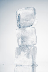 The vertical stack of three ice cubes on white background with reflection.