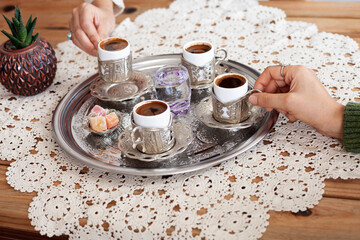 Women holding Turkish and Greek coffee cups inside metal tray, lace cover on wooden table