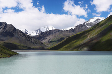 A serene blue lake surrounded by towering snow-capped mountains. A body of water among the green...