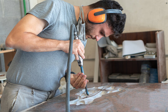 Caucasian man sculptor, bush hammering a granite headstone in a workshop, work concept
