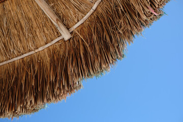 Low angle shot of the edge of a tiki parasol and the blue sky