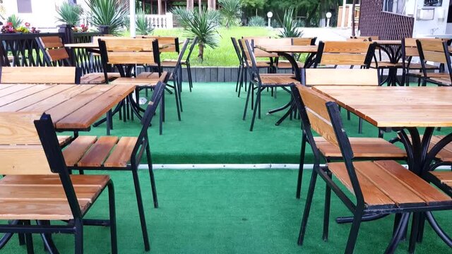 Slow movement of the camera in an empty street cafe past wooden tables and chairs and green carpet, 4 k video