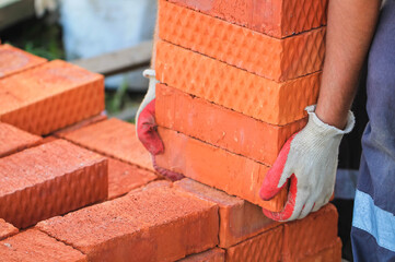 Photo of a worker at a construction site. Red brick in the hands of a builder.