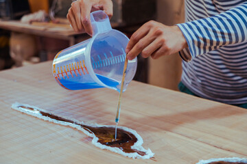 Closeup of carpenter pouring liquid epoxy in a wooden table