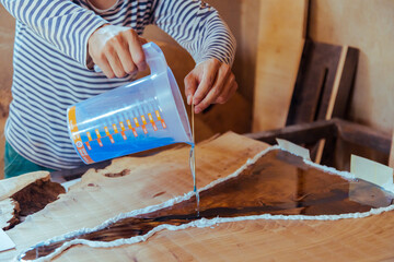 Closeup of carpenter pouring liquid epoxy in a wooden table