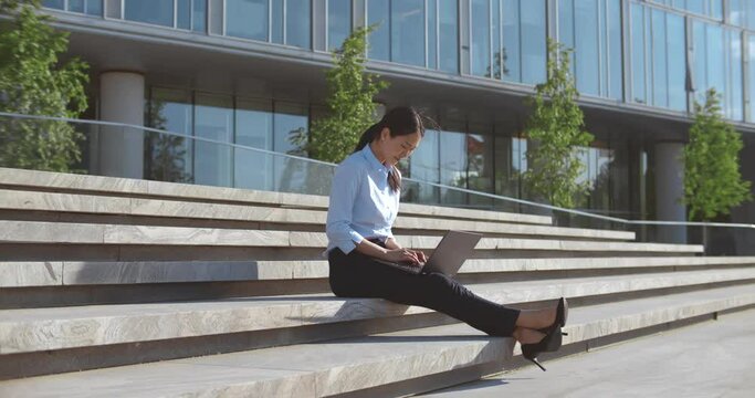 Young asian businesswoman using laptop computer on stairs outdoors