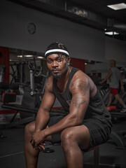 Fototapeta na wymiar African american male fitness instructor sitting on bench. Handsome powerful athletic man in stylish sportswear in gym
