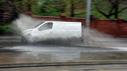 Samochód w czasie ulewy wpada w kałużę wody na jezdni powodując rozbryzg. - obrazy, fototapety, plakaty