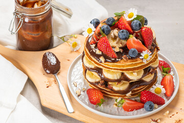 Obraz na płótnie Canvas Pancakes with chocolate paste and hazelnuts, banana, strawberry and blueberry