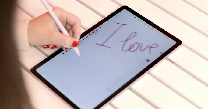 In love woman writing I love you on a digital tablet with a technological stylus for his partner. Valentine's day celebration.