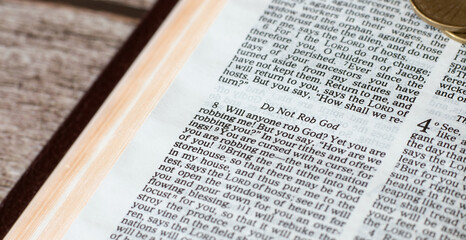 The biblical concept of tithing and generosity. Give your tithe to God Jesus Christ. Golden money on a wooden table with Holy Bible. Finances, donations, giving offerings, and blessings. A closeup.