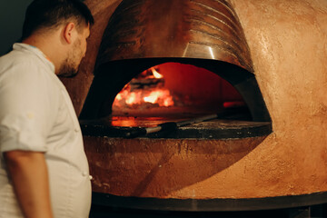 The chef prepares pizza in a wood-fired oven. Cooking pizza. The cook puts the pizza in the oven.