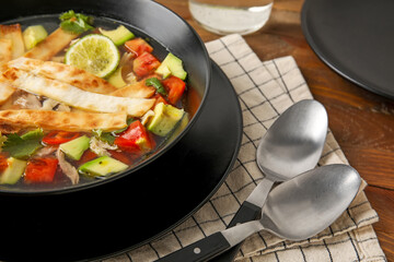 Bowl of tasty Sopa de Lima soup on wooden background, closeup