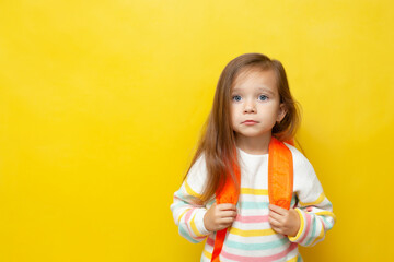 Portrait of a sad girl with a backpack. European appearance. Emotions. Back to school. The child does not want to go to school. Learning difficulties. Academic year. Yellow background, space for text.
