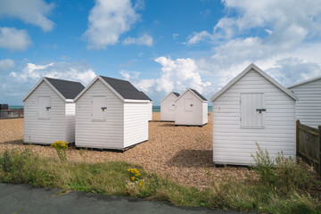Fototapeta na wymiar White beach huts on a pebble beach with a blue sky and white clouds.