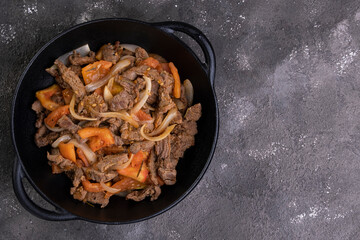 Sliced and fried filet mignon with tomato and onion in an iron skillet