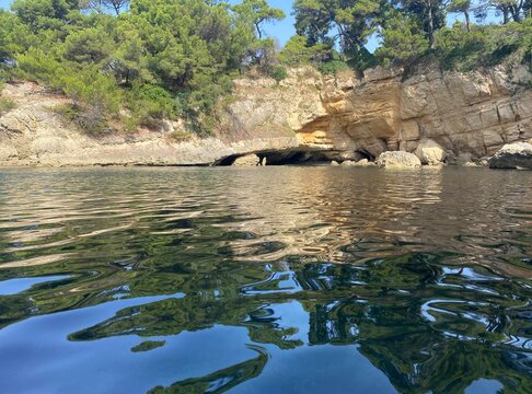 Sea lagoon with cave grotto on rocky coast at summer. Secluded place for relax. Pine trees on cliff. Beautiful landscape of seaside. Calm clear water.  Scenic nature of Mediterranean coast.