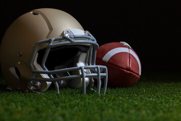 Low angle selective focus of football and gold helmet on grass with dark background