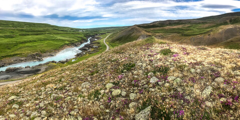 Panorama of green fields and stones and a river among the valley of Iceland.
