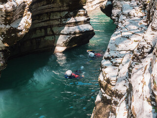 Two men in helmets and wetsuits float down a turquoise river into a canyon gorge. Overcoming water...