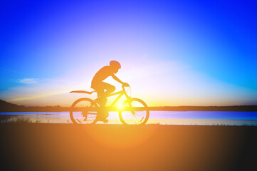Obraz premium Unrecognizable silhouette man riding bicycle against sunset sky. Road biking cyclist workout, riding racing bicycle on open road. Workout for triathlon. Dramatic sunset background. side view
