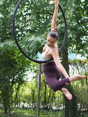 Junge Frau trainiert Pole Dance Sport draußen im Garten, wobei ihr ganzer Körper hängt und mit...