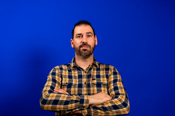 Young man standing crossed arms looks annoyed with frowning face emotion on a blue background.