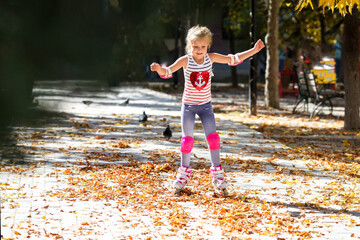Little girl on roller skates and tram protection riding in the autumn park. Healthy lifestyle concept.